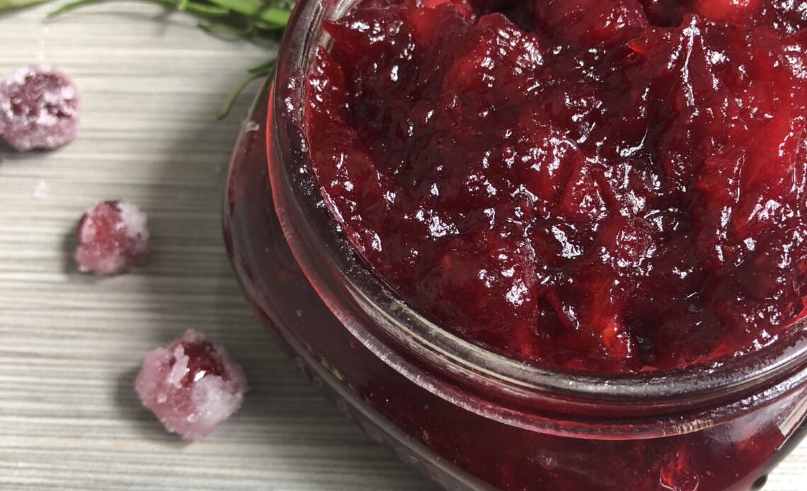 Holiday Cranberry Sauce in a mason jar with a silver spoon and accented with sugared cranberries and fresh rosemary
