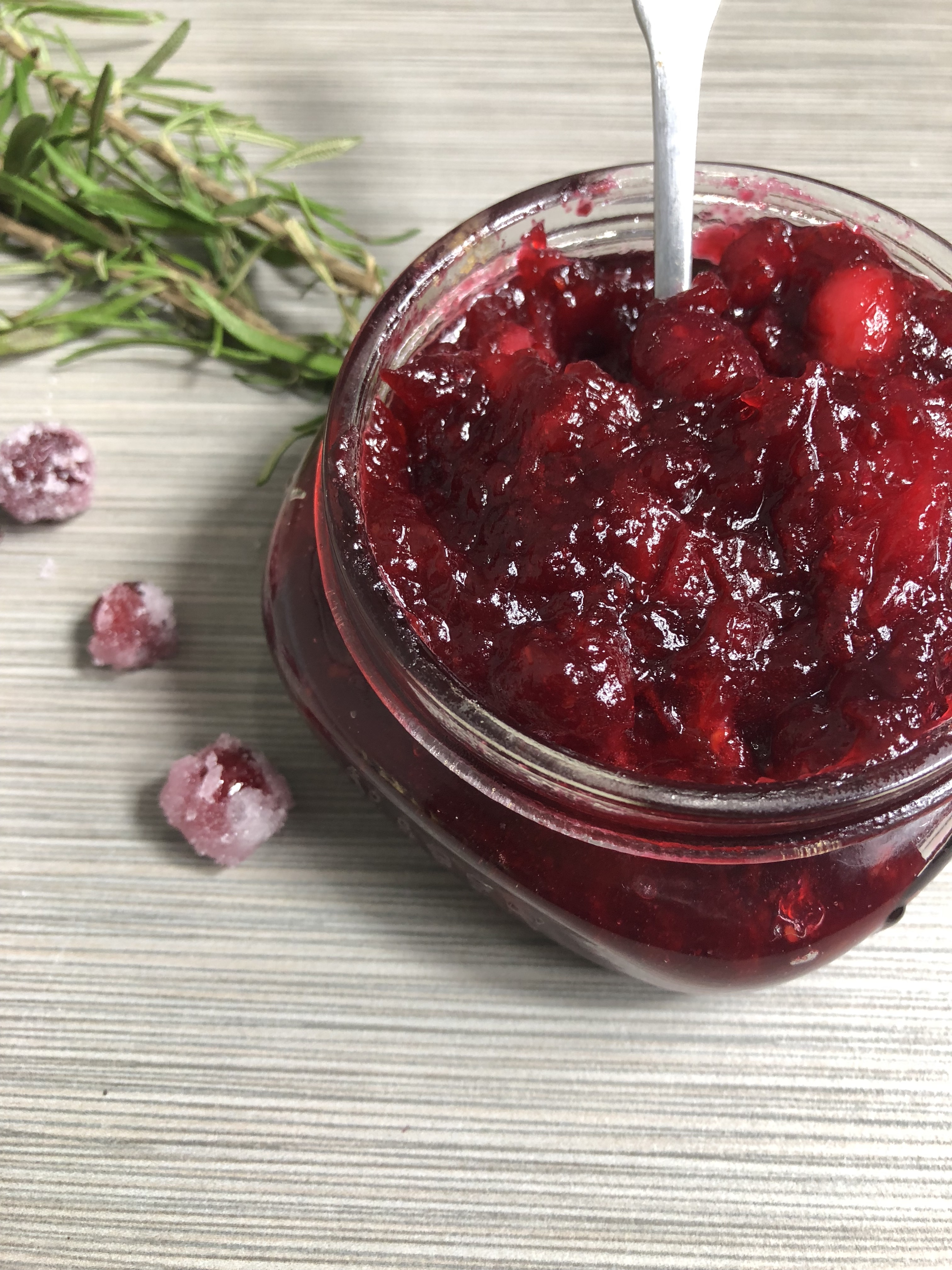 Holiday Cranberry Sauce in a mason jar with a silver spoon and accented with sugared cranberries and fresh rosemary