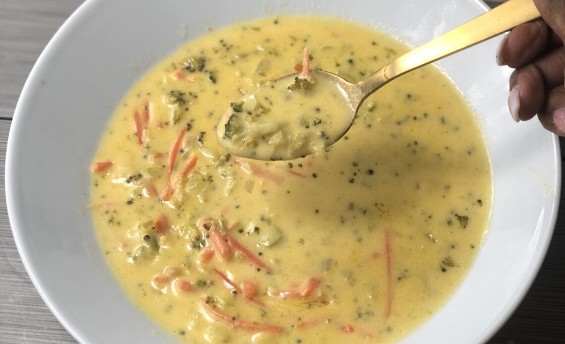 A bowl of broccoli cheddar soup and a golden spoon.