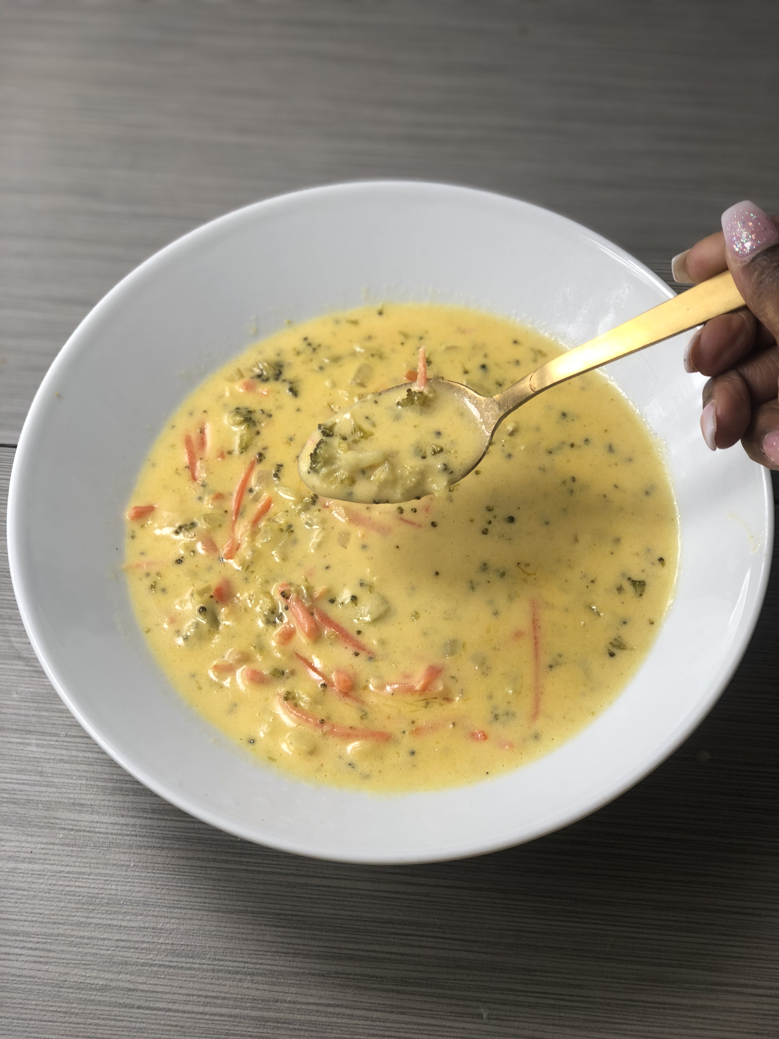 A bowl of broccoli cheddar soup and a golden spoon.