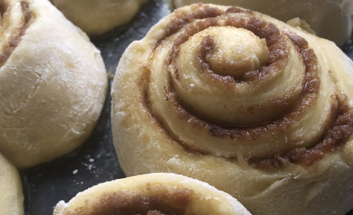 Homemade cinnamon rolls lined up in a glass pan and ready for baking.