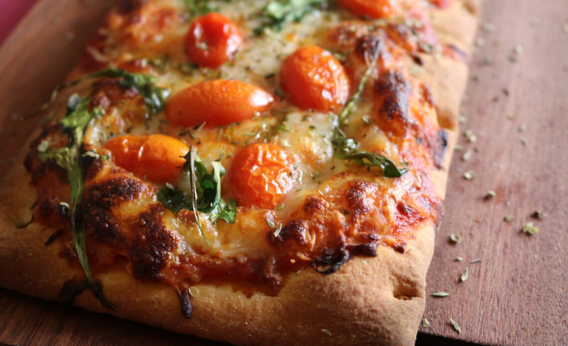 Flatbread pizza topped with tomatoes arugula and Italian spices on a dark wood board
