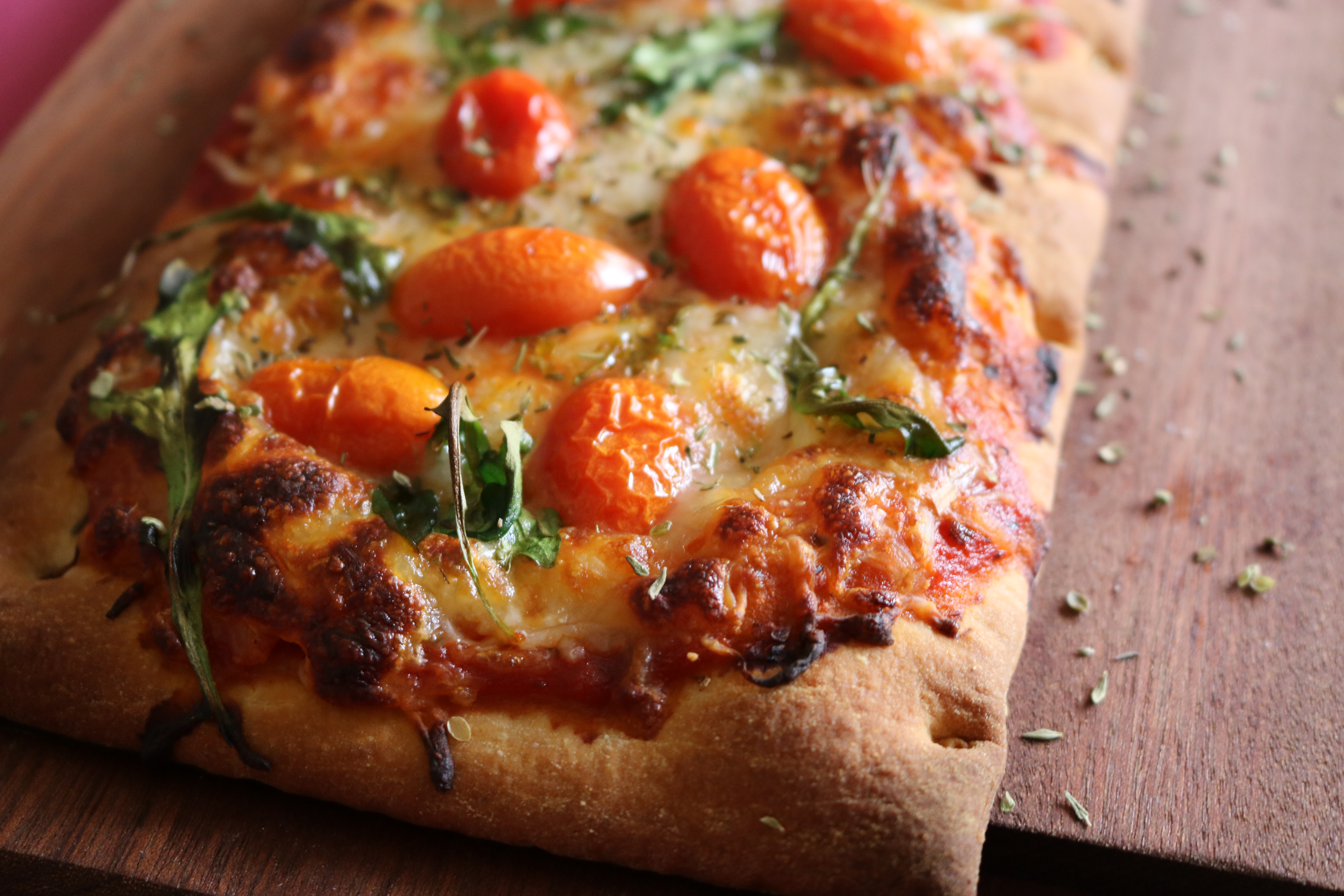Flatbread pizza topped with tomatoes arugula and Italian spices on a dark wood board