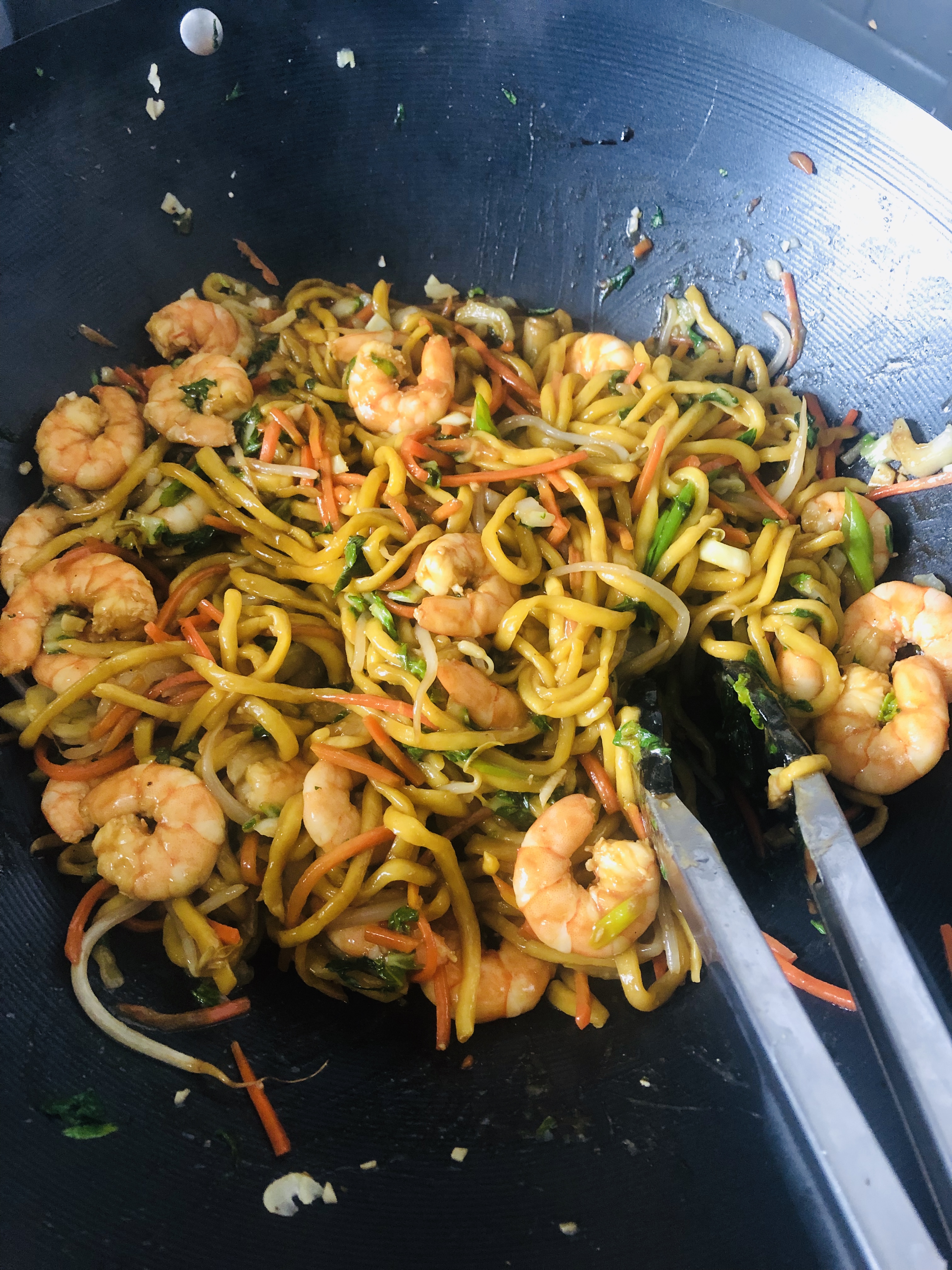 A mound of Chinese lo mein topped with shrimp and veggies in a large non-stick wok