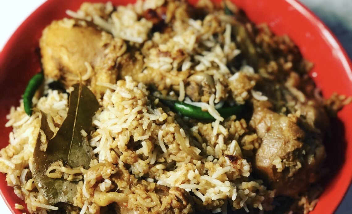 A bowl of rice, chicken, chili peppers and bay leaves.