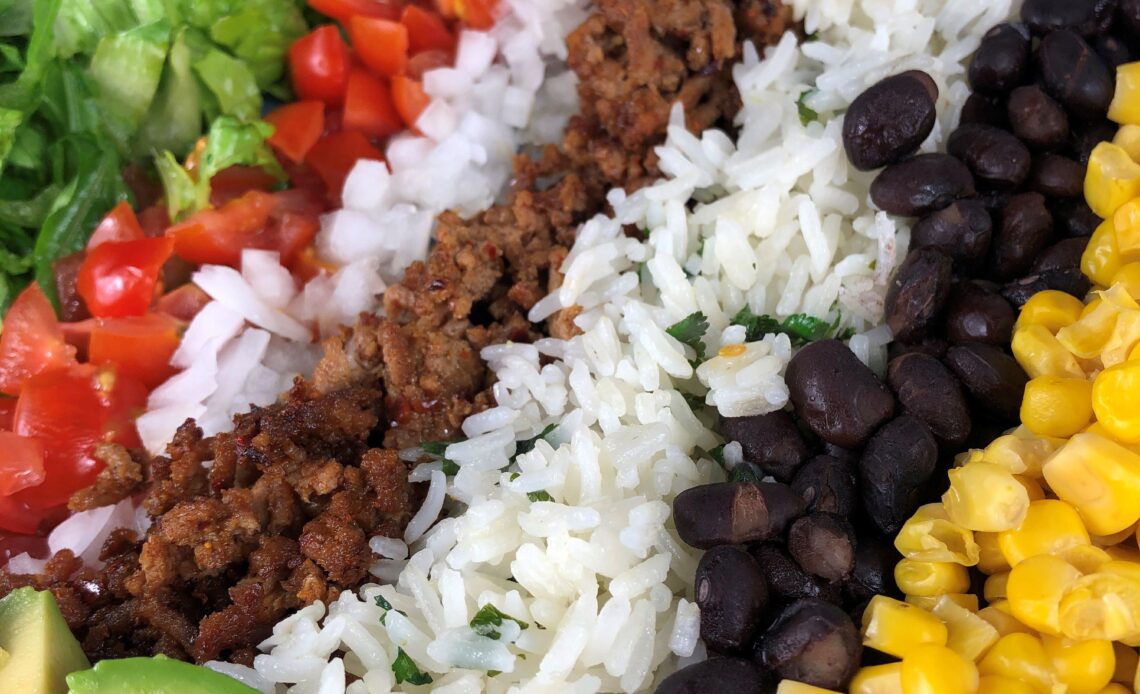 A burrito bowl filled with chopped lettuce, tomatoes, onion, seasoned ground turkey, cilantro rice, black beans, corn, avocado and fresh queso blanco.
