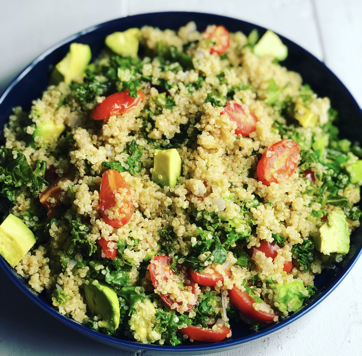 Quinoa, avocado, grape tomatoes, and kale in a dark blue plate.