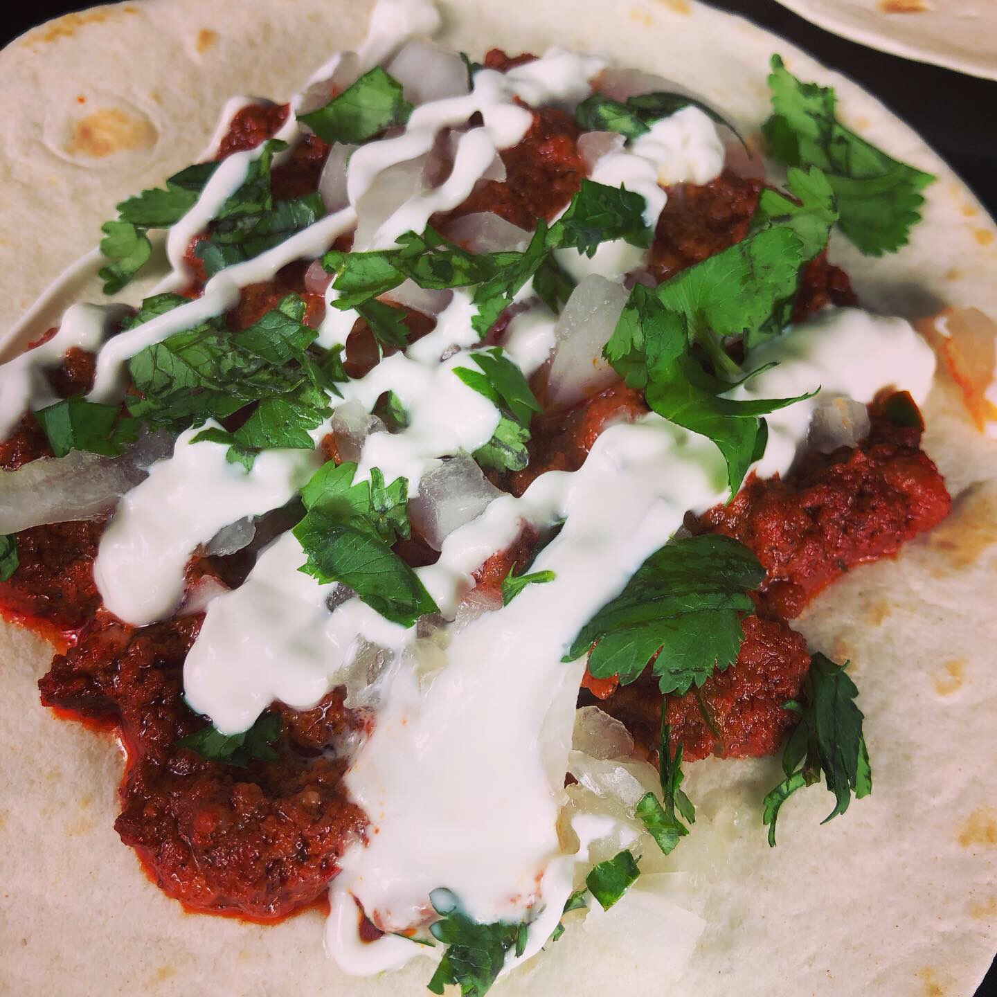 Flour tortilla topped with chorizo, diced onion, chopped cilantro, and a sour cream lime sauce