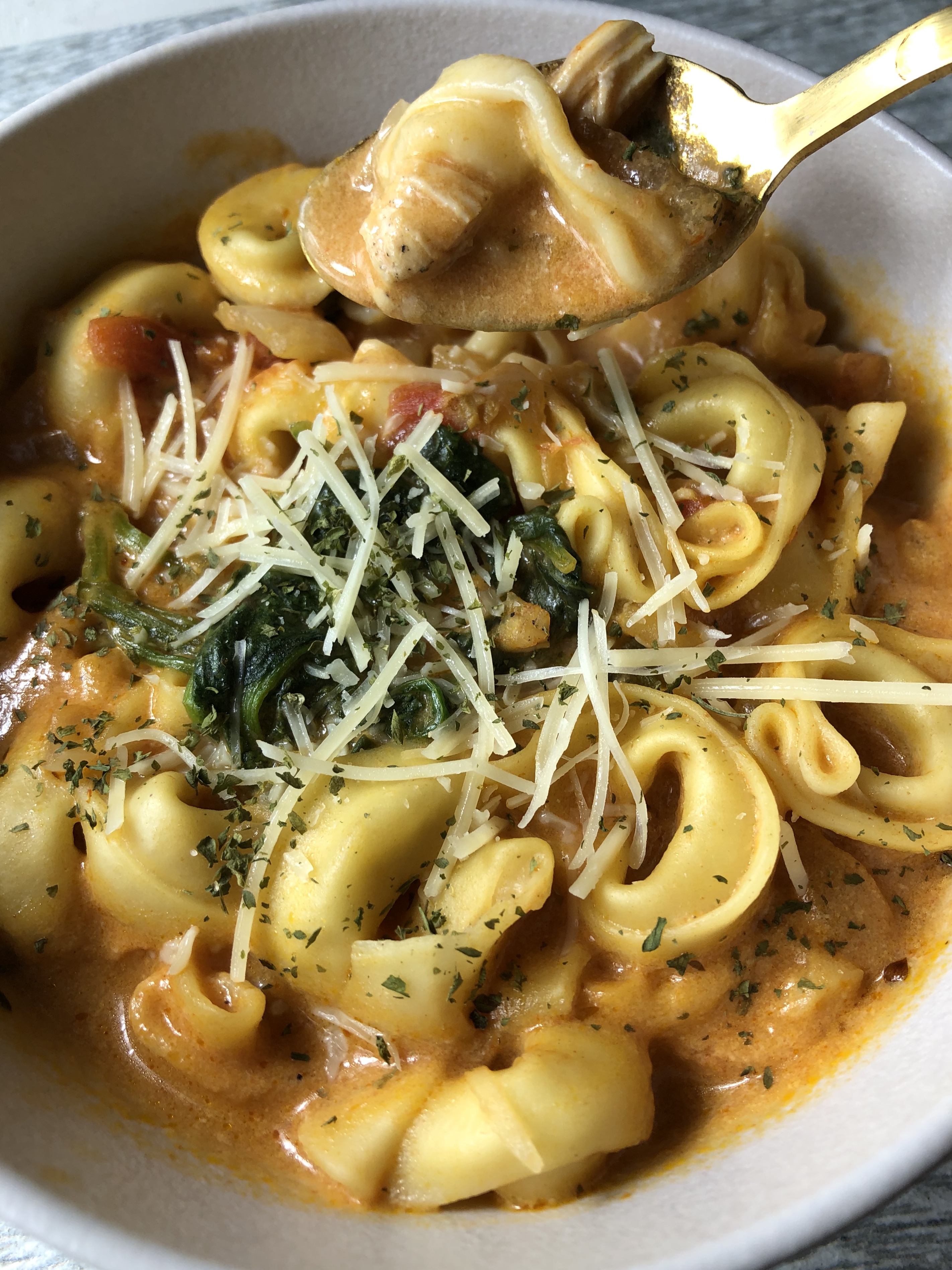 Eggshell colored bowl filled with creamy chicken tortellini soup topped with spinach and Parmesan cheese