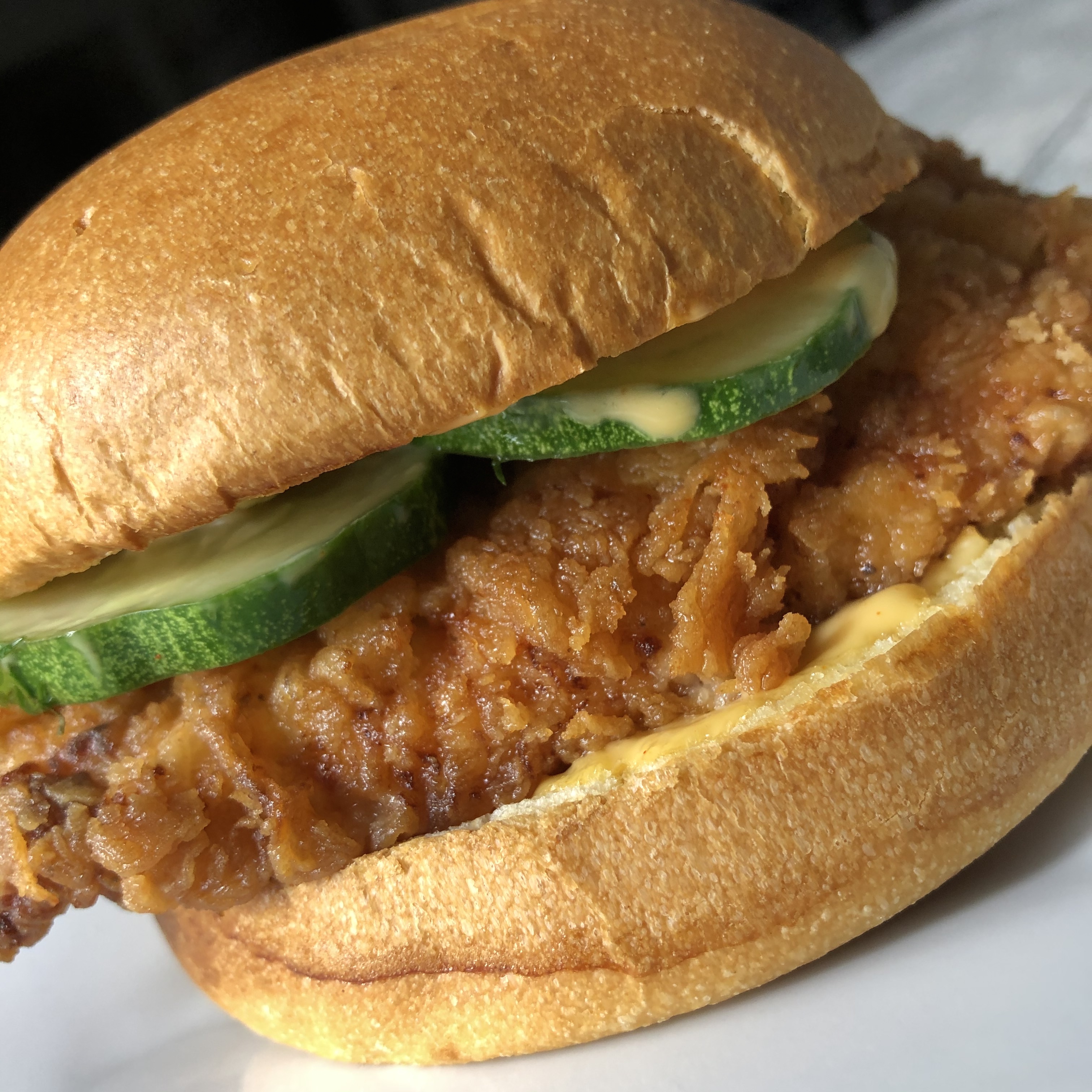 Close up view of a crispy fried chicken breast topped with dill pickles on a brioche bun