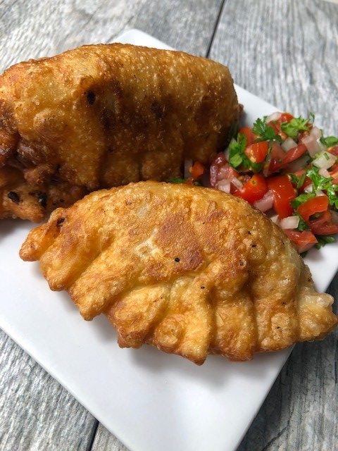 Thanksgiving Turkey Empanadas served with pico de gallo on a square, white plate positioned on a light gray tabel.