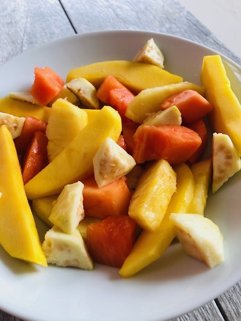 Chopped mango, papaya, pineapple and guava in a white bowl against a wood grain background.