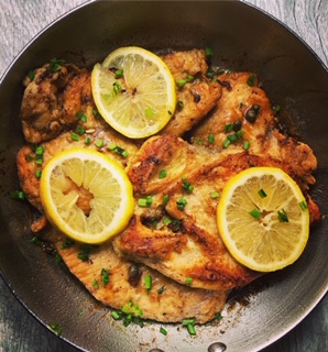 Pan fried chicken breasts topped with lemon rounds and chopped chives in a lemon oil sauce