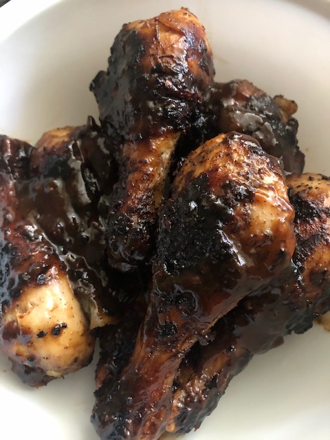 Grilled Jerk Chicken Drumsticks tossed in jerk BBQ sauce in a white mixing bowl.