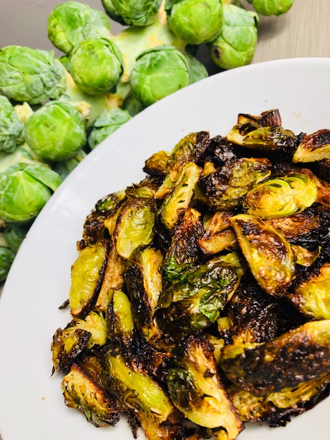 Roasted Brussels sprouts in a white porcelain bowl with a Brussels sprouts stalk in the background.