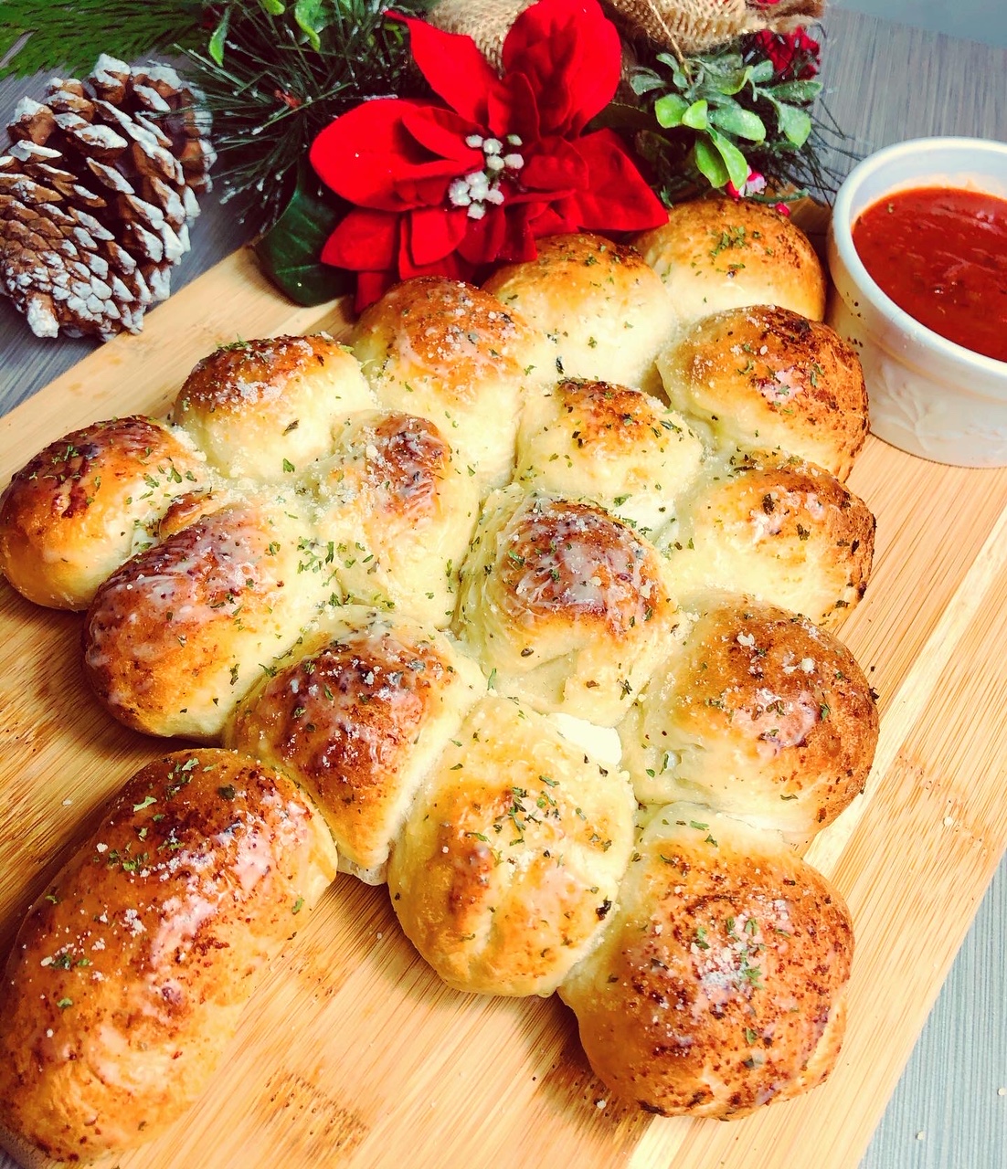 Mozzarella cheese stuffed bread, browned to perfection, shaped into a Christmas tree pyramid, brushed with garlic herb butter, served on a wooden cutting board accented with frosted pine cones and poinsettias.