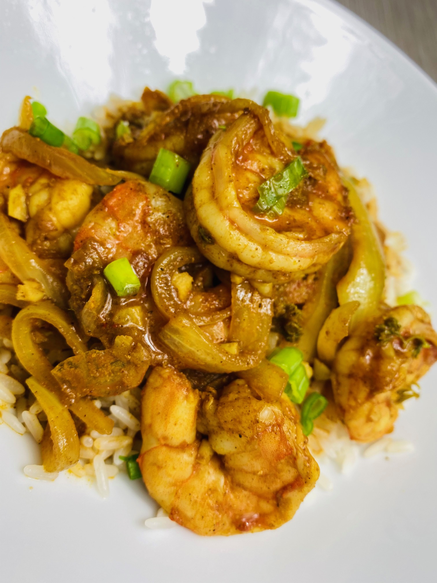 Curry Shrimp in a spicy curry sauce served on a bed of steamed white rice in a white porcelain bowl and sprinkled with chopped scallion