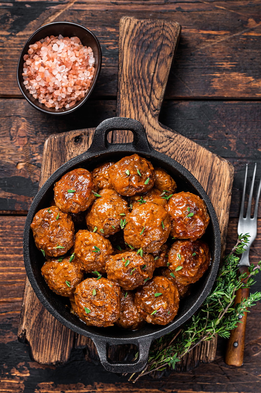 Pan-seared lamb meatballs with thyme in cast iron pan. Dark background. Top view